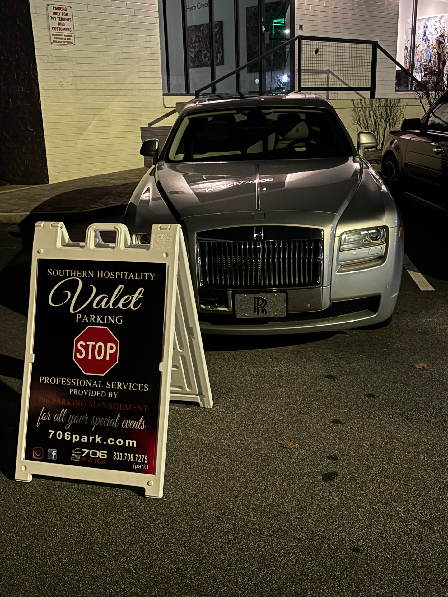 706 Park valet sign in front of a silver Rolls-Royce Ghost parked at night