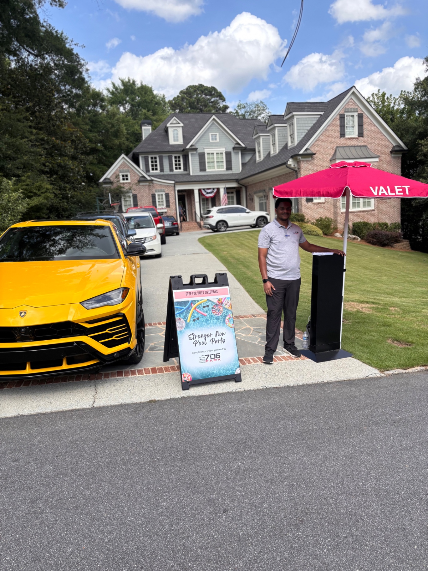 706 Park valet attendant at a valet stand under a red umbrella beside a yellow Lamborghini Urus at a suburban Atlanta home